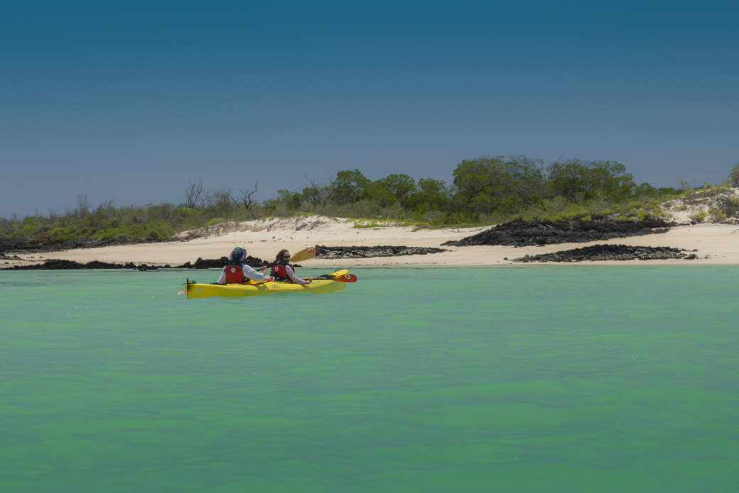 Kayaking couple approaches white sand beach on Galapagos kayaking tour